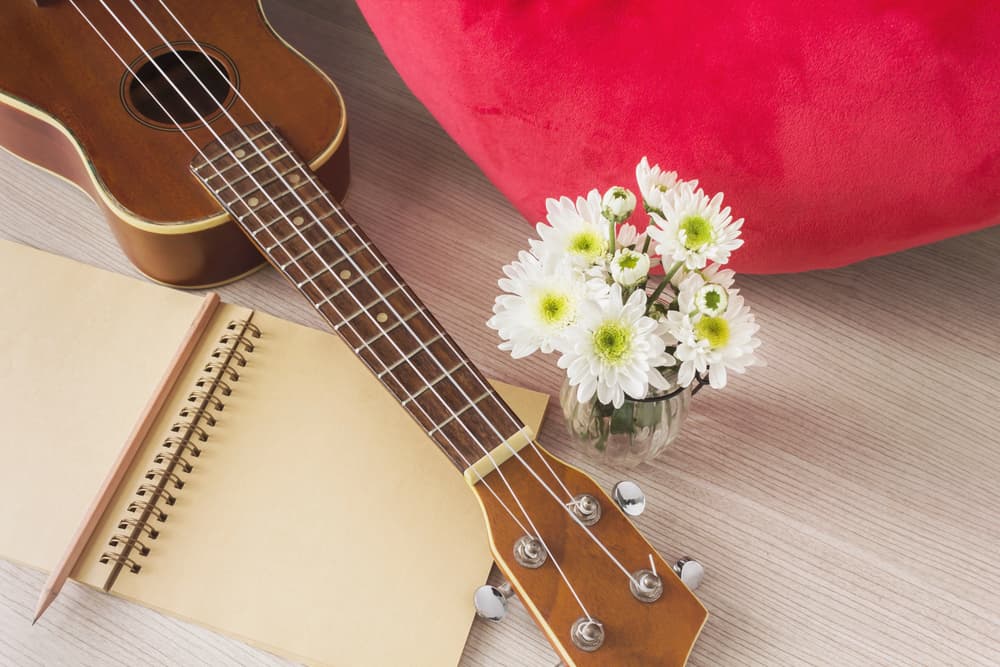 Ukulele on desk with notebook and white flowers
